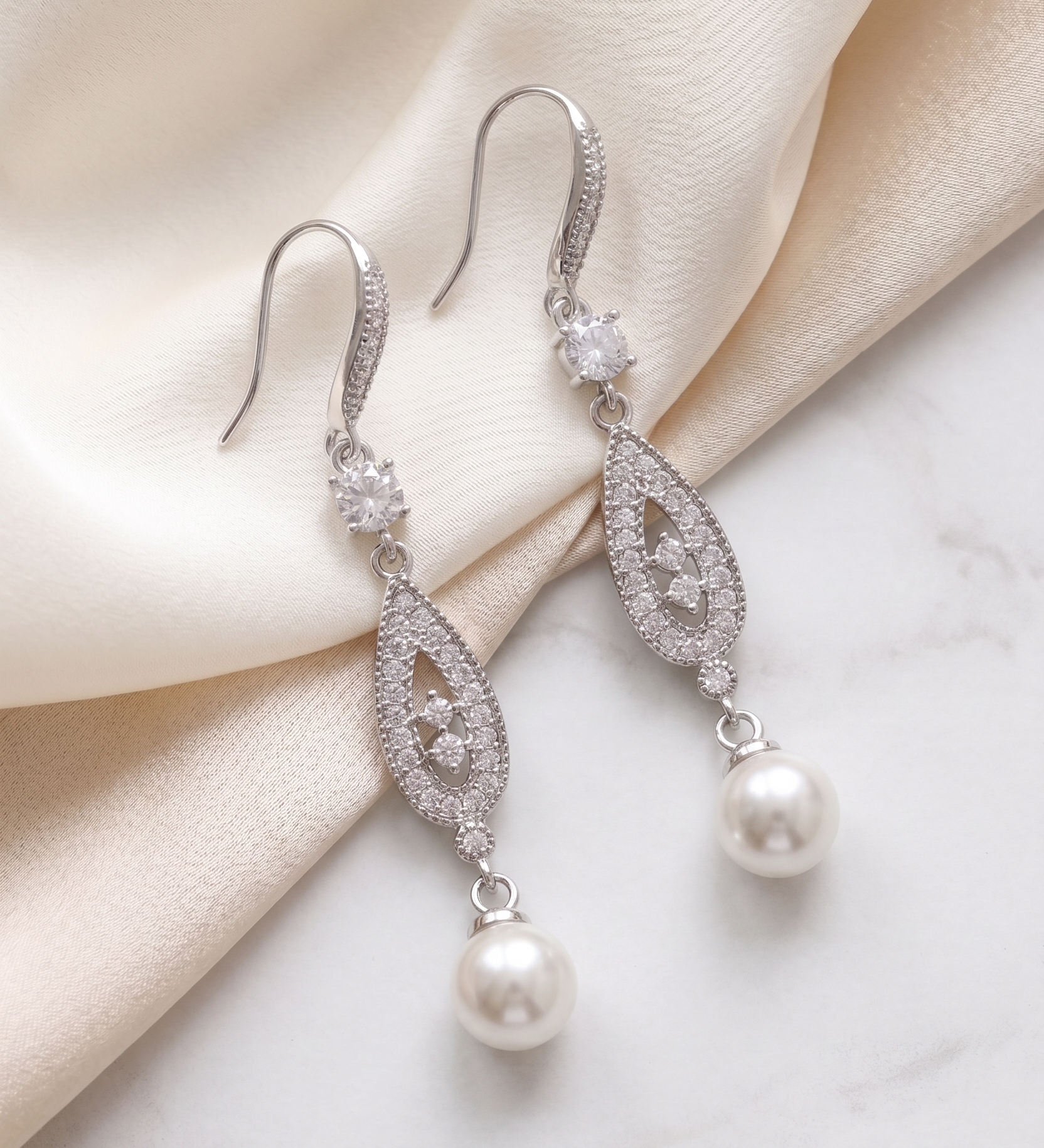 A pair of elegant earrings with pearls and diamonds resting on a white marble surface.