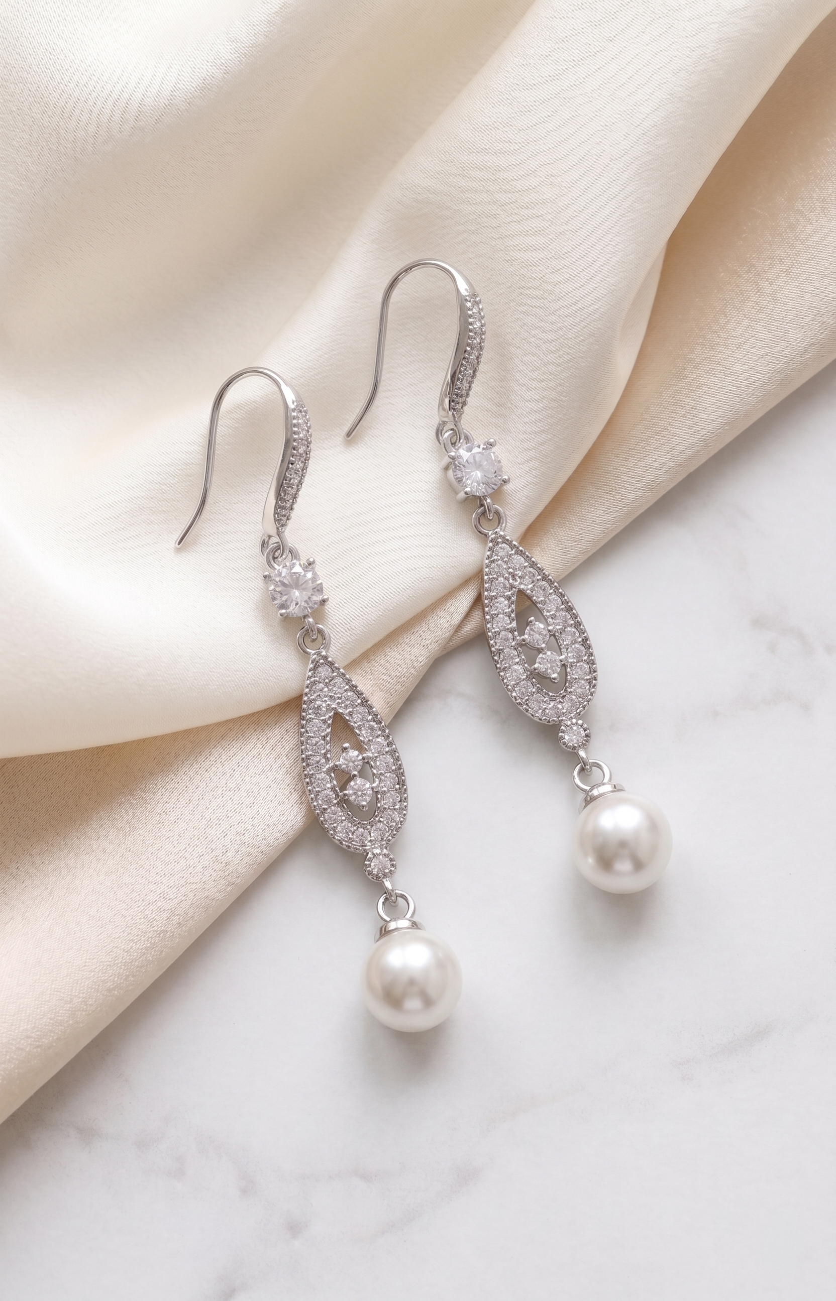 A pair of elegant earrings with pearls and diamonds resting on a white marble surface.