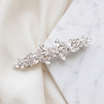 A decorative hair clip with a floral design and sparkling crystal elements rests on a white marble surface.