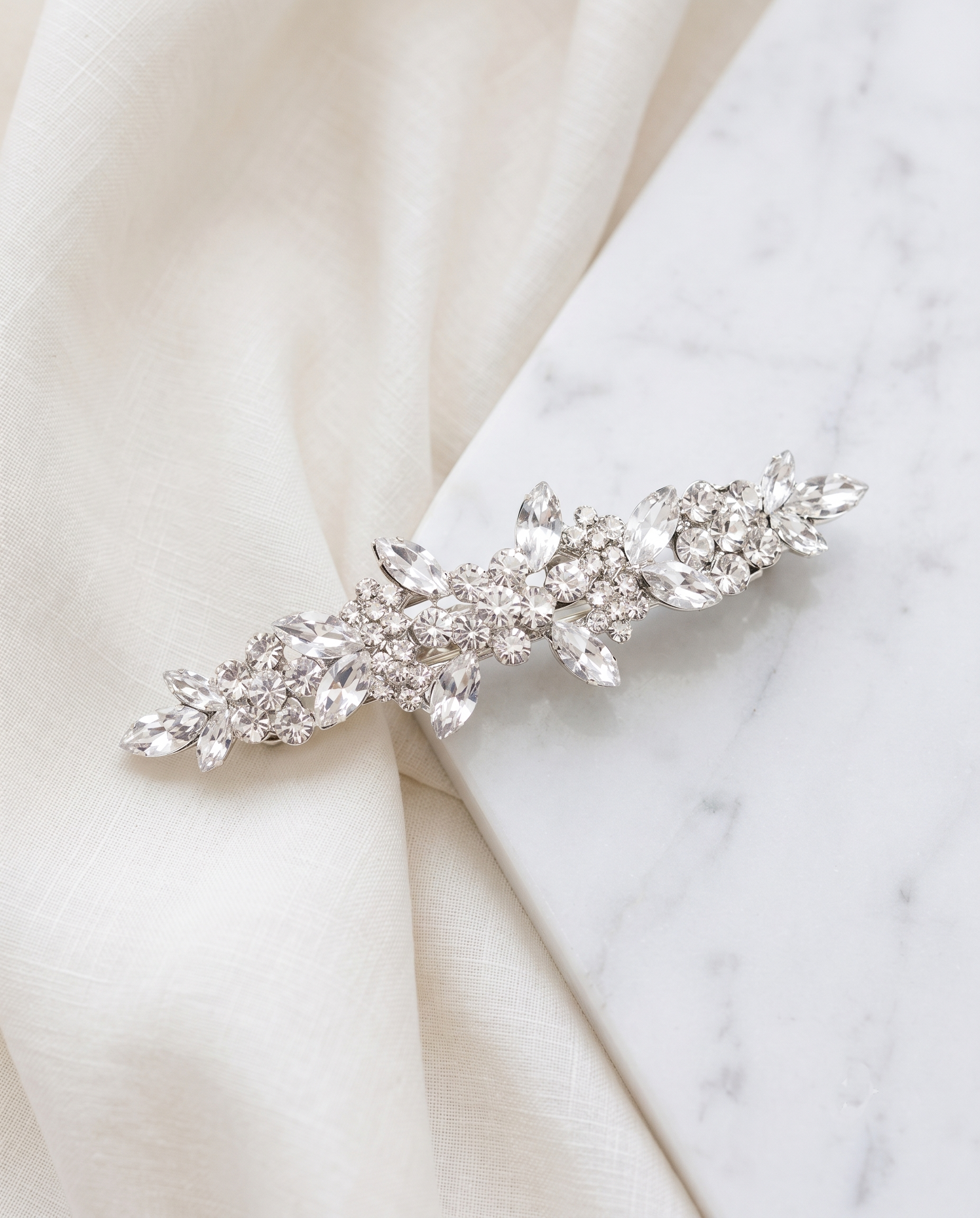 A decorative hair clip with a floral design and sparkling crystal elements rests on a white marble surface.