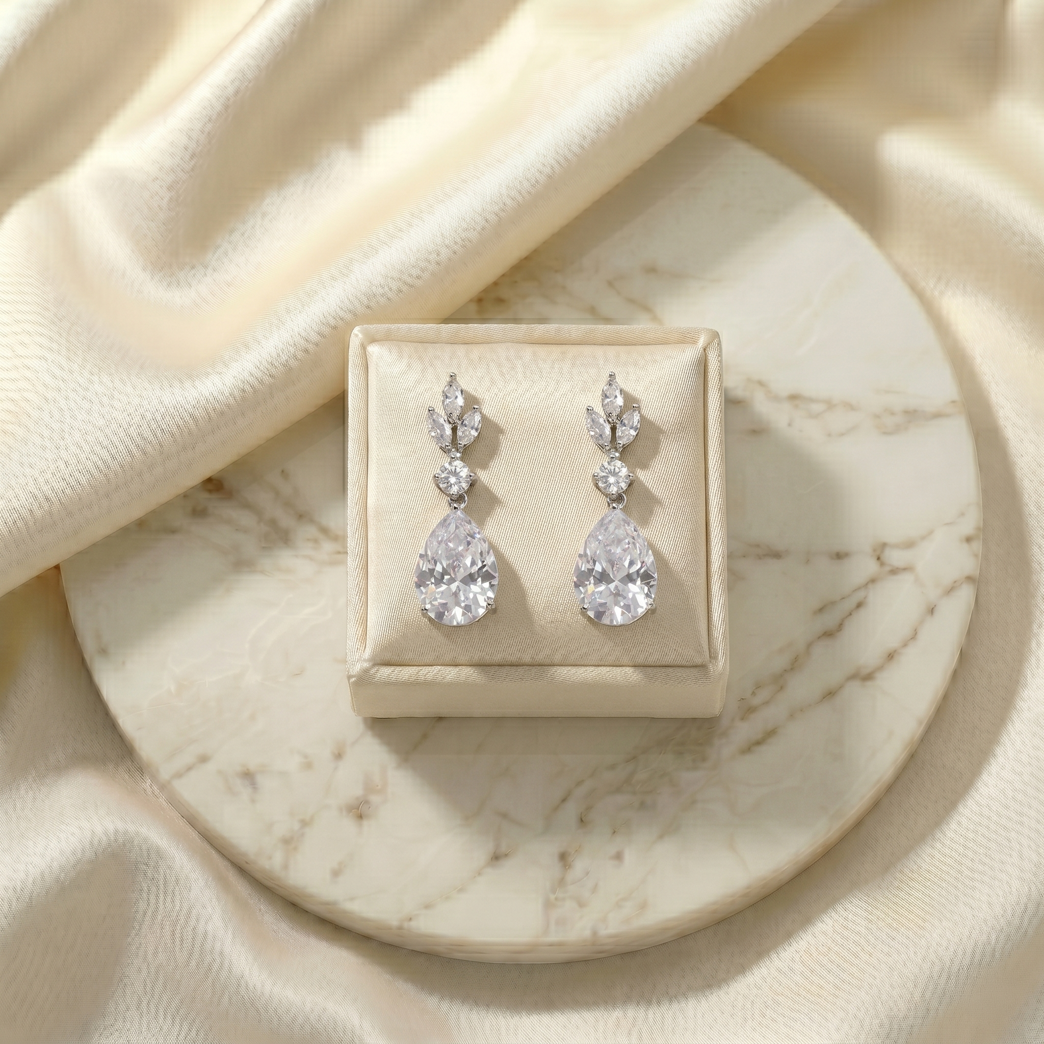 A pair of elegant diamond earrings is displayed on a white marble surface, placed in a small white box.