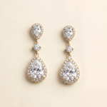 A pair of elegant gold earrings with large, clear gemstones set in a halo around the center of each earring.