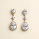 A pair of elegant gold earrings with large, clear gemstones set in a halo around the center of each earring.