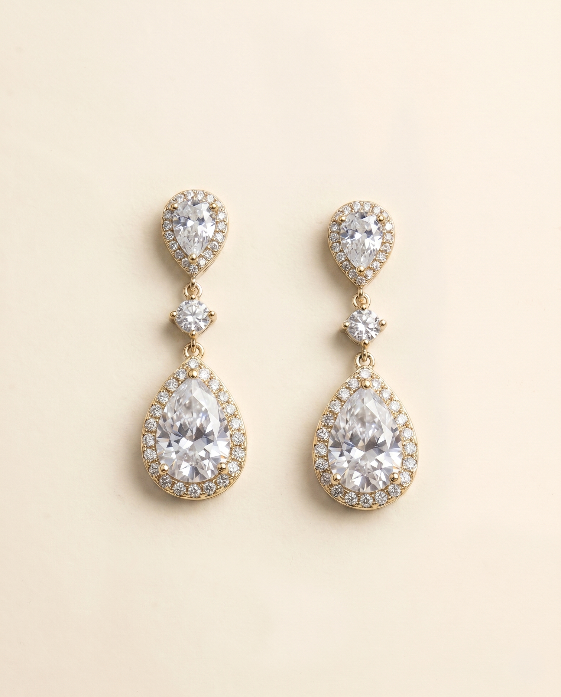 A pair of elegant gold earrings with large, clear gemstones set in a halo around the center of each earring.