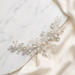 A decorative piece of jewelry, possibly a necklace or bracelet, adorned with small pearls and crystals, resting on a white marble surface.