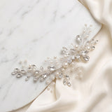 A decorative piece of jewelry, possibly a necklace or bracelet, adorned with small pearls and crystals, resting on a white marble surface.