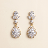 A pair of elegant gold earrings with large, clear gemstones set in a halo-like design.