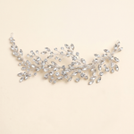 A decorative piece of jewelry with a branch-like design, adorned with numerous small, clear gemstones.