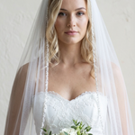 A woman in a white wedding dress holding a bouquet of white roses stands against a plain white background.