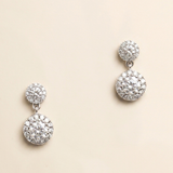 A pair of elegant diamond earrings with a large central stone surrounded by smaller stones, set in a silver or white metal frame.