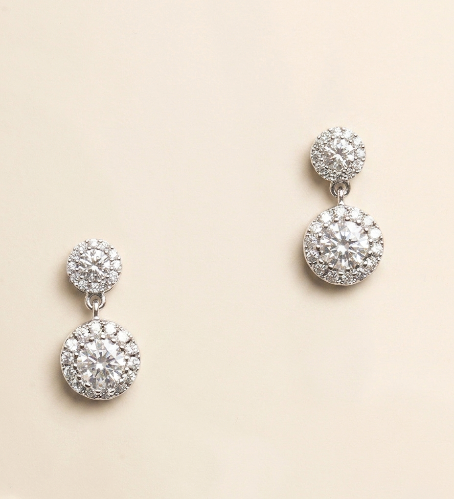 A pair of elegant diamond earrings with a large central stone surrounded by smaller stones, set in a silver or white metal frame.