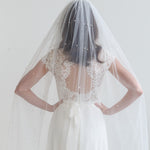 A woman wearing a white wedding dress with a veil, standing against a white background.