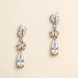 A pair of elegant gold earrings with clear gemstones, including pear-shaped and teardrop-shaped stones, hanging from the ear hooks.