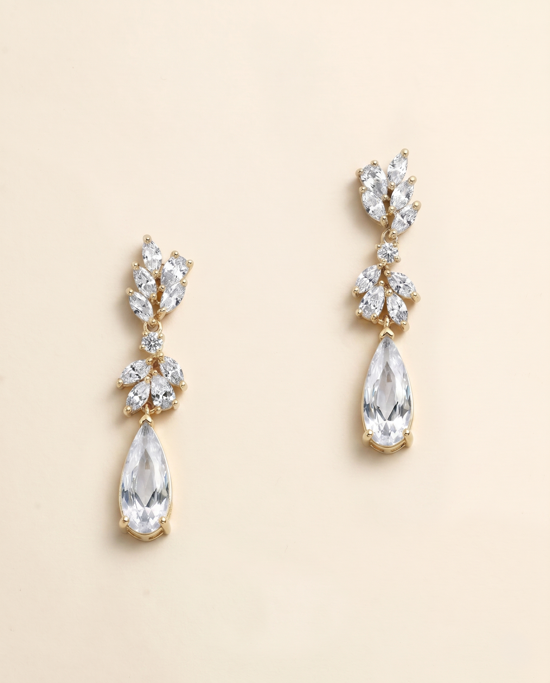 A pair of elegant gold earrings with clear gemstones, including pear-shaped and teardrop-shaped stones, hanging from the ear hooks.