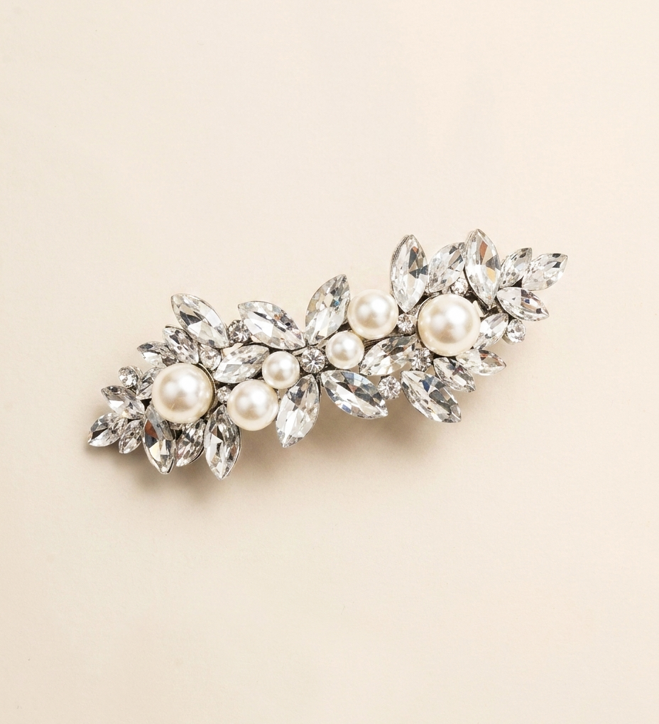 A decorative hair clip adorned with numerous sparkling crystal elements, including pearls and diamonds, set against a light beige background.