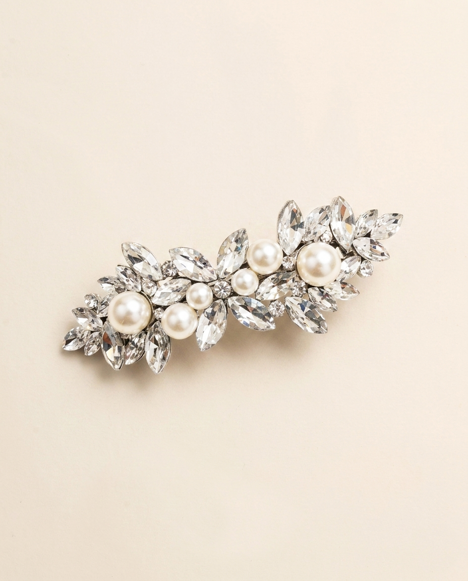 A decorative hair clip adorned with numerous sparkling crystal elements, including pearls and diamonds, set against a light beige background.