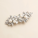 A decorative hair clip adorned with numerous sparkling crystal elements, including pearls and diamonds, set against a light beige background.