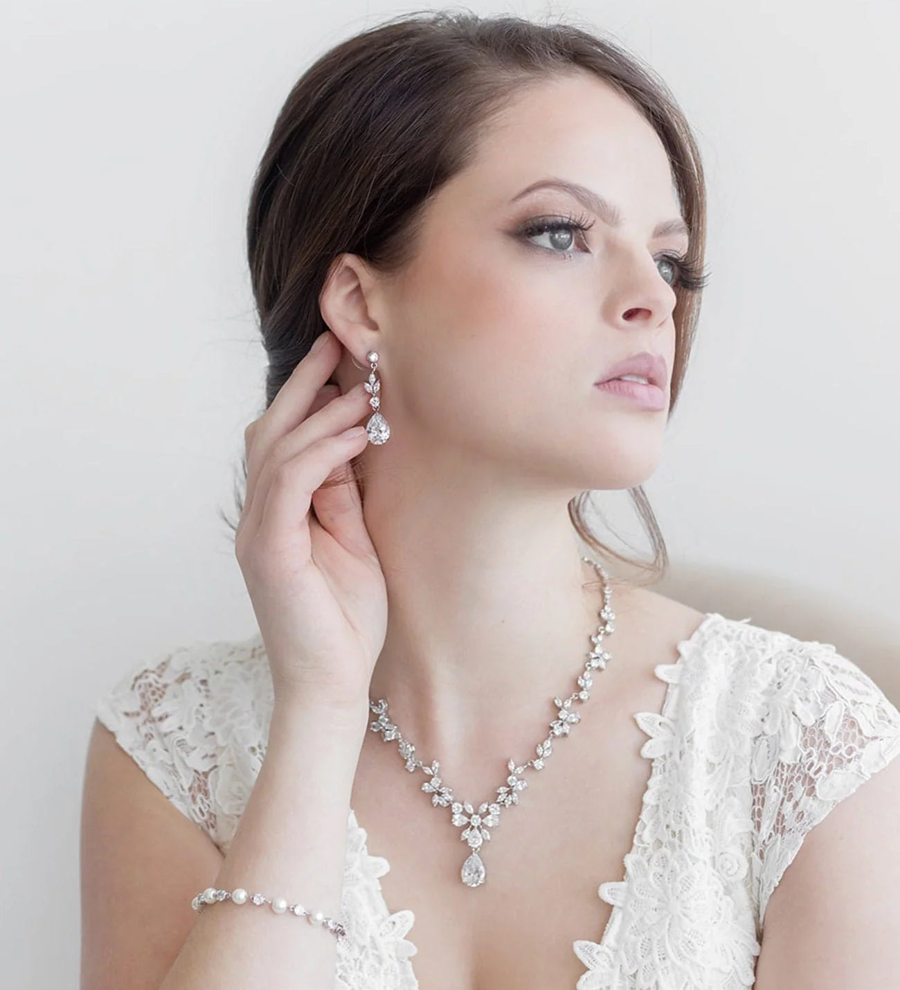 A woman in a white lace dress and diamond jewelry poses against a plain white background.