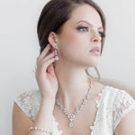 A woman in a white lace dress and diamond jewelry poses against a plain white background.