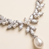 A close-up view of a delicate necklace with a large pearl pendant and a cluster of sparkling crystal stones.