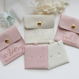 a collection of pink and white bridesmaid bags with personalized names on them, along with some white flowers and a white fabric background.