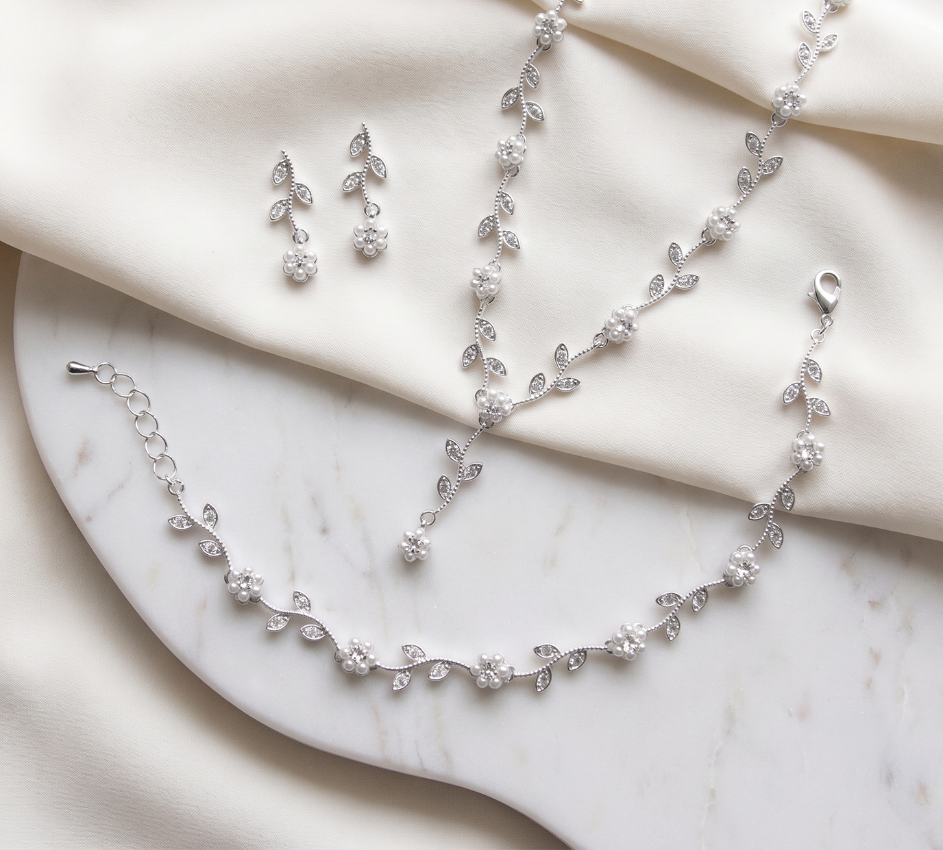 A delicate necklace, bracelet, and earrings are arranged on a white marble surface, creating an elegant and sophisticated display.