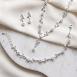 A delicate necklace, bracelet, and earrings are arranged on a white marble surface, creating an elegant and sophisticated display.