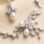 A close-up image of a delicate necklace and earrings set, featuring a combination of pearls and diamonds.