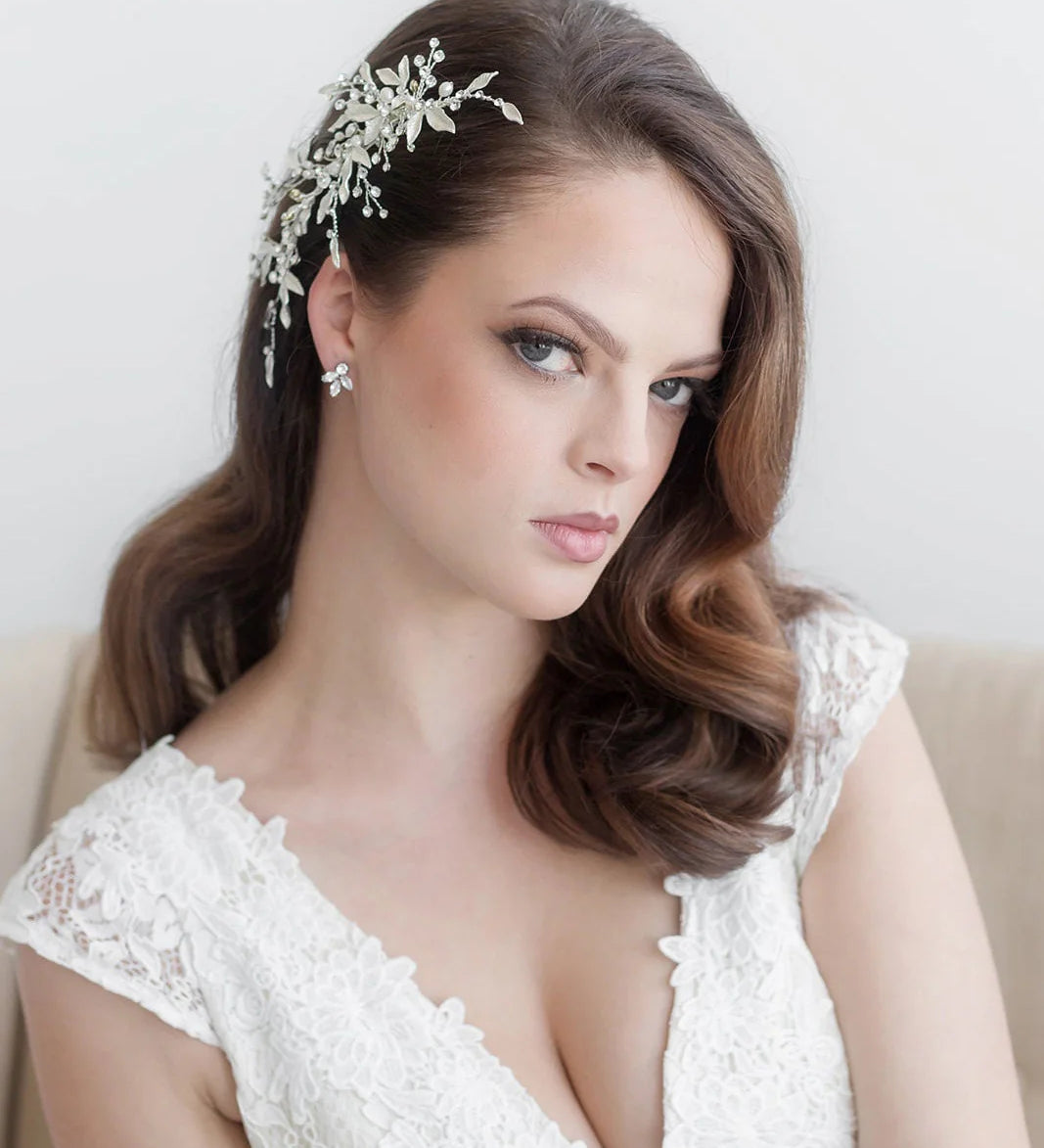 A woman with long brown hair wearing a white lace dress and a decorative headpiece, looking directly at the camera with a serious expression.