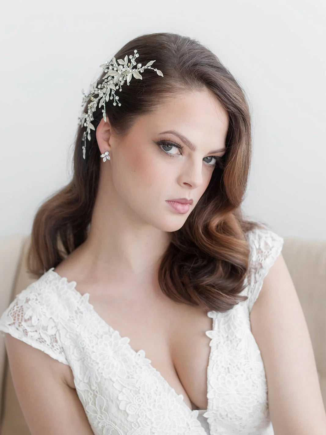 A woman with long brown hair wearing a white lace dress and a decorative headpiece, looking directly at the camera with a serious expression.