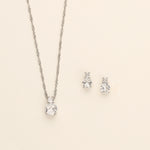 A silver necklace with a pendant and two diamond earrings are displayed against a light background.