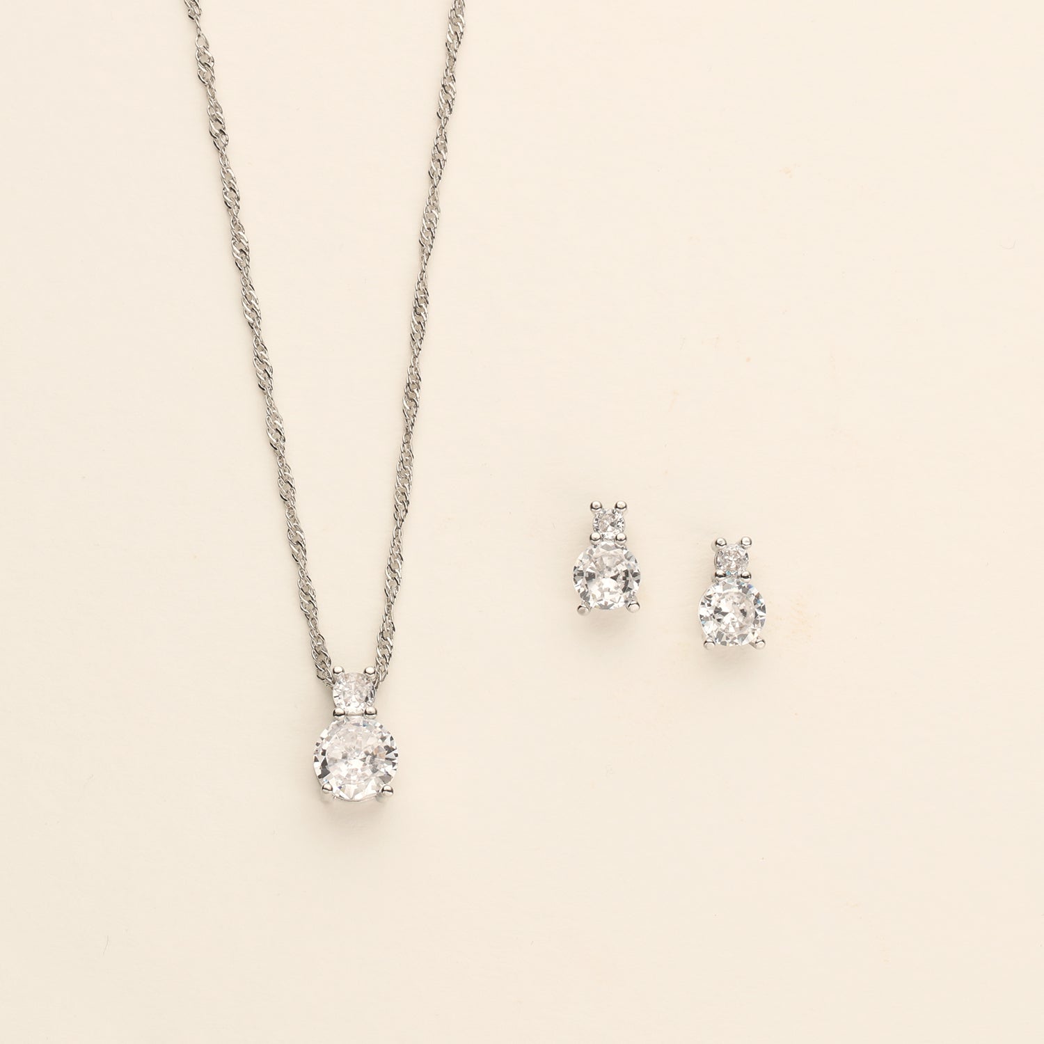 A silver necklace with a pendant and two diamond earrings are displayed against a light background.