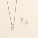 A silver necklace with a pendant and two diamond earrings are displayed against a light background.