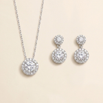 A necklace with a pendant and a pair of earrings with a central stone are displayed against a light beige background.