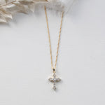 A gold cross pendant necklace with small diamonds is displayed against a white background.