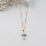 A gold cross pendant necklace with small diamonds is displayed against a white background.