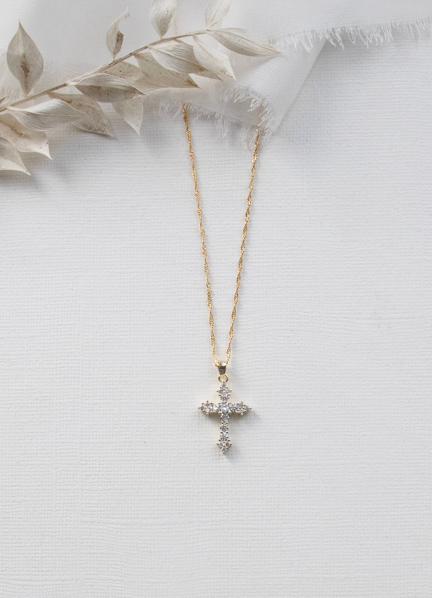 A gold cross pendant necklace with small diamonds is displayed against a white background.