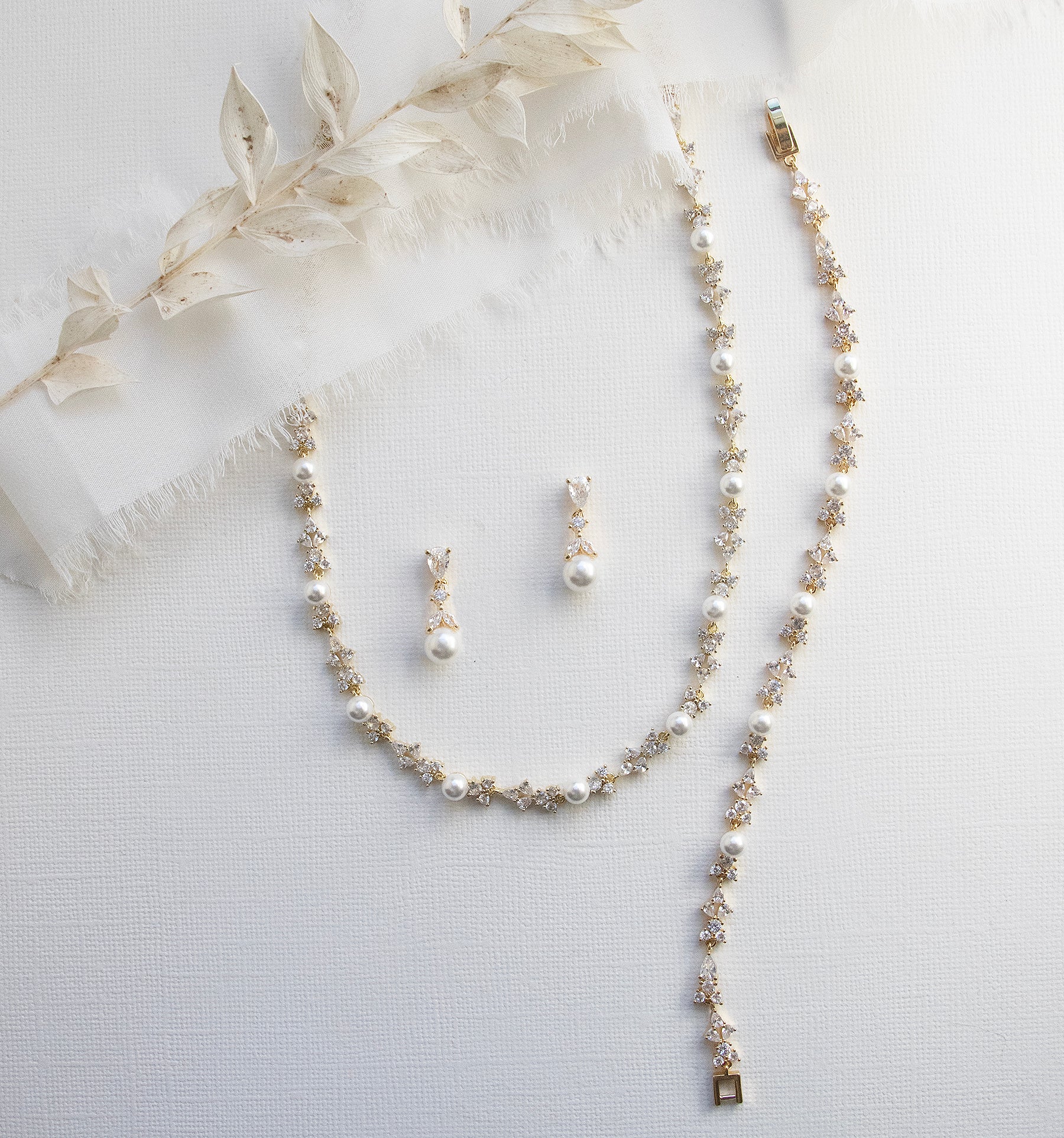 A delicate necklace with a long chain and a pair of earrings with pearls are displayed on a white background.