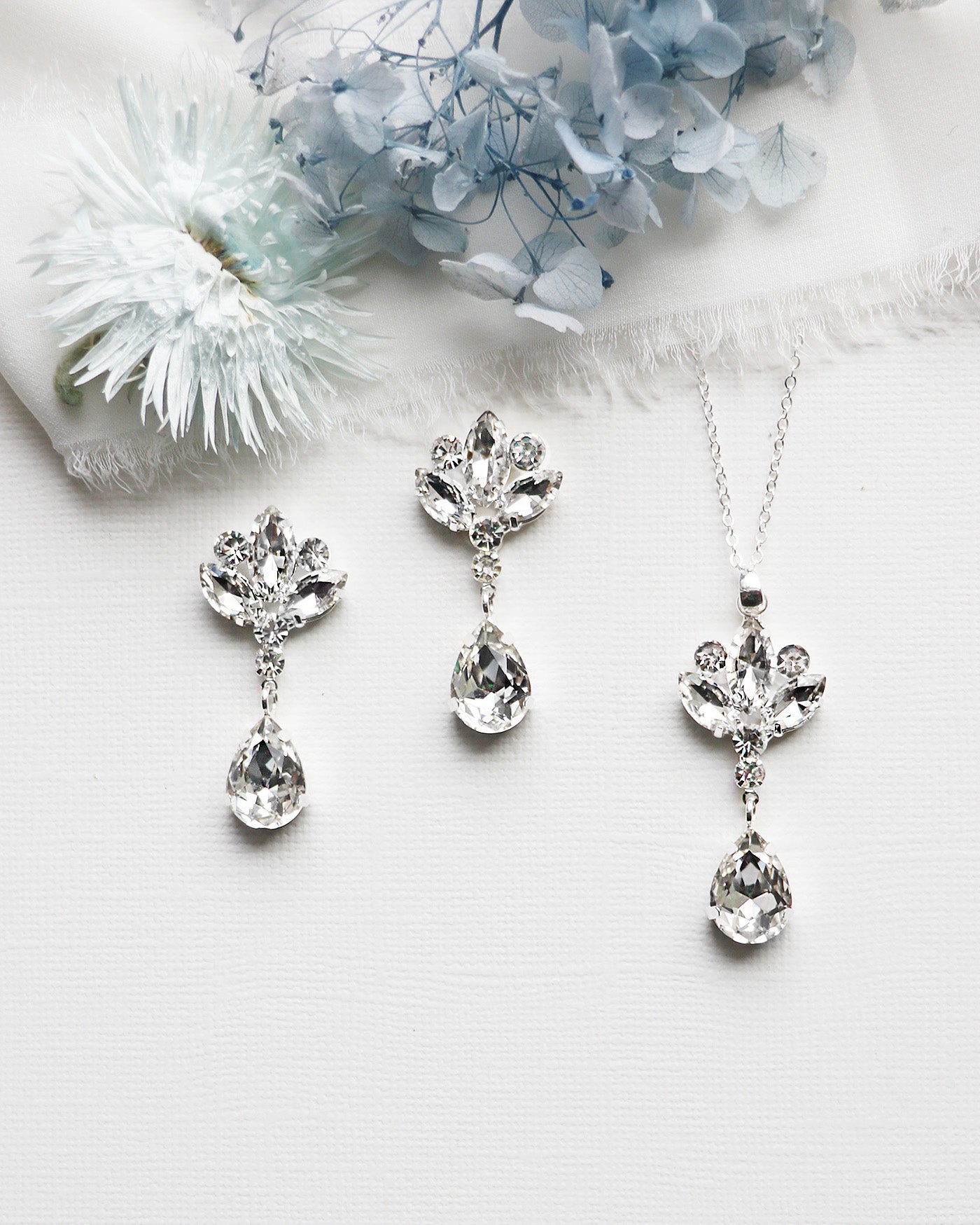 a necklace, earrings, and flower on a white surface