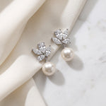 A pair of elegant earrings with a pearl and crystal embellishment, resting on a white fabric surface.