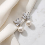 A pair of elegant earrings with a pearl and crystal embellishment, resting on a white fabric surface.