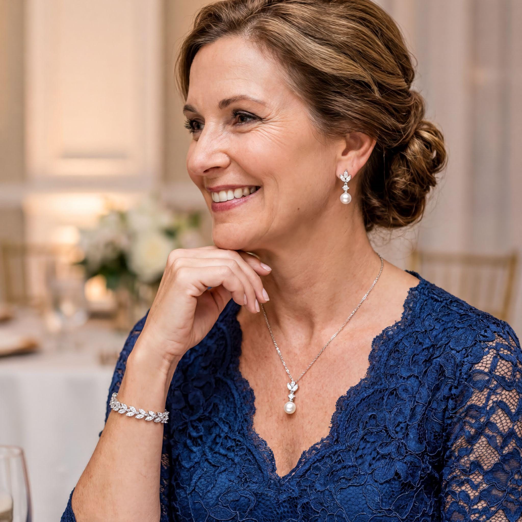 A woman in a blue lace dress with a pearl necklace and earrings is smiling and looking to the side.