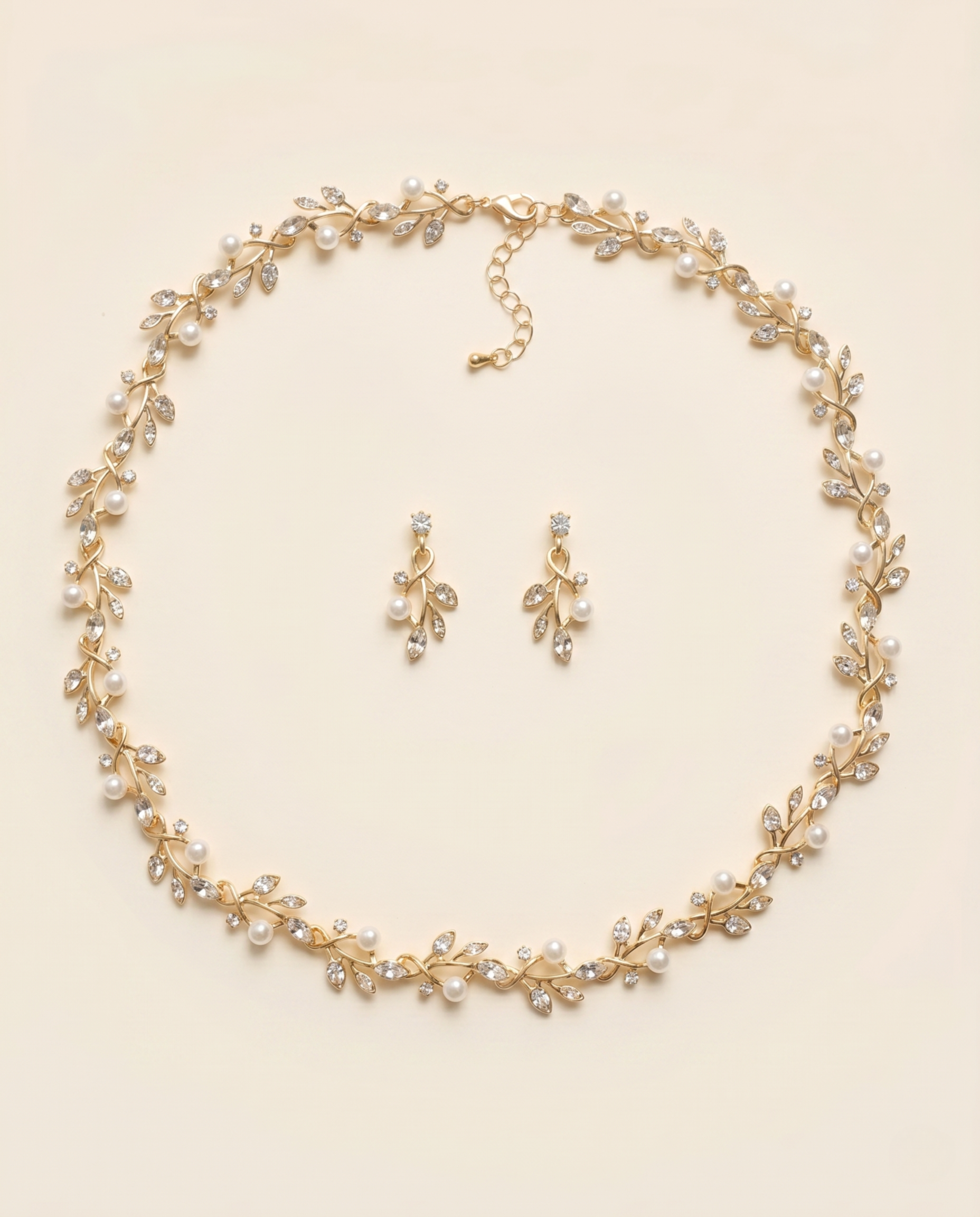 A delicate gold necklace with a leaf-shaped pendant and a pair of dangling earrings are arranged in a circular pattern on a light-colored background.