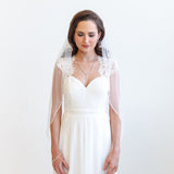 A woman in a white wedding dress with a veil stands against a white background, looking down with a thoughtful expression.