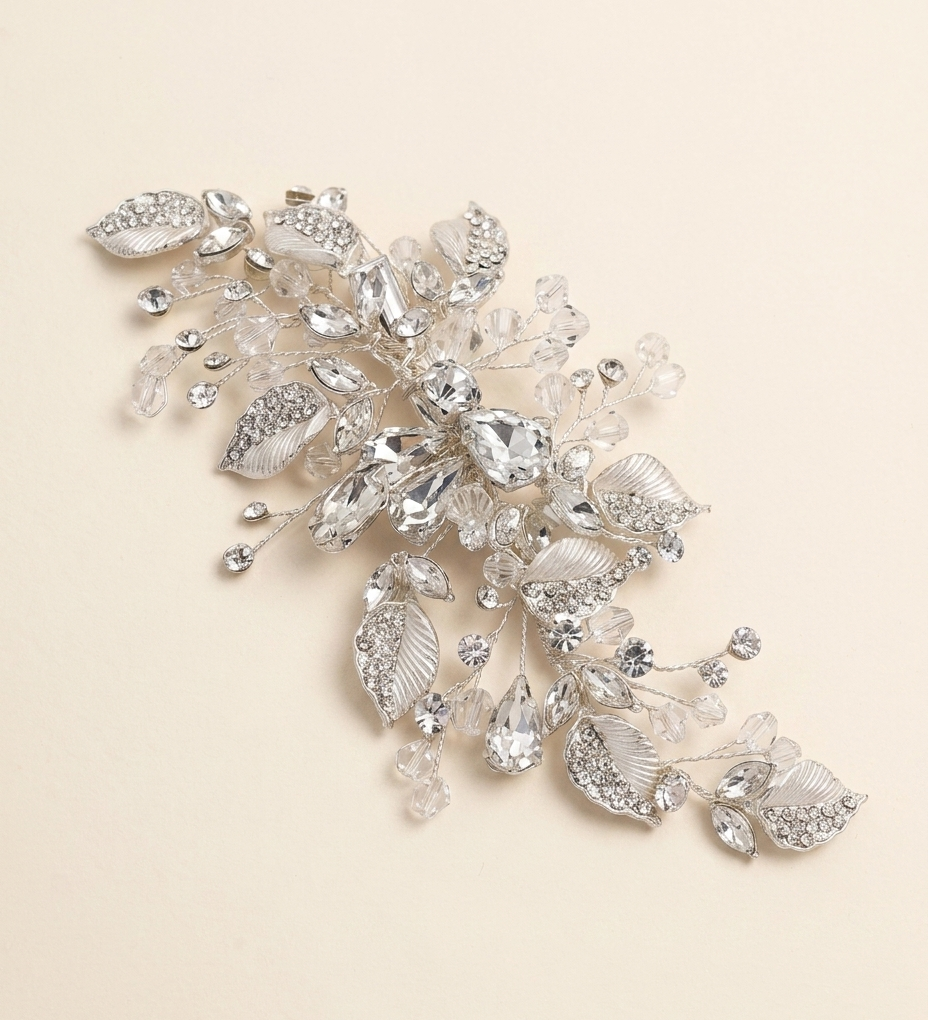 A decorative piece of jewelry with a combination of clear and silver elements, including leaves and crystals, set against a light beige background.