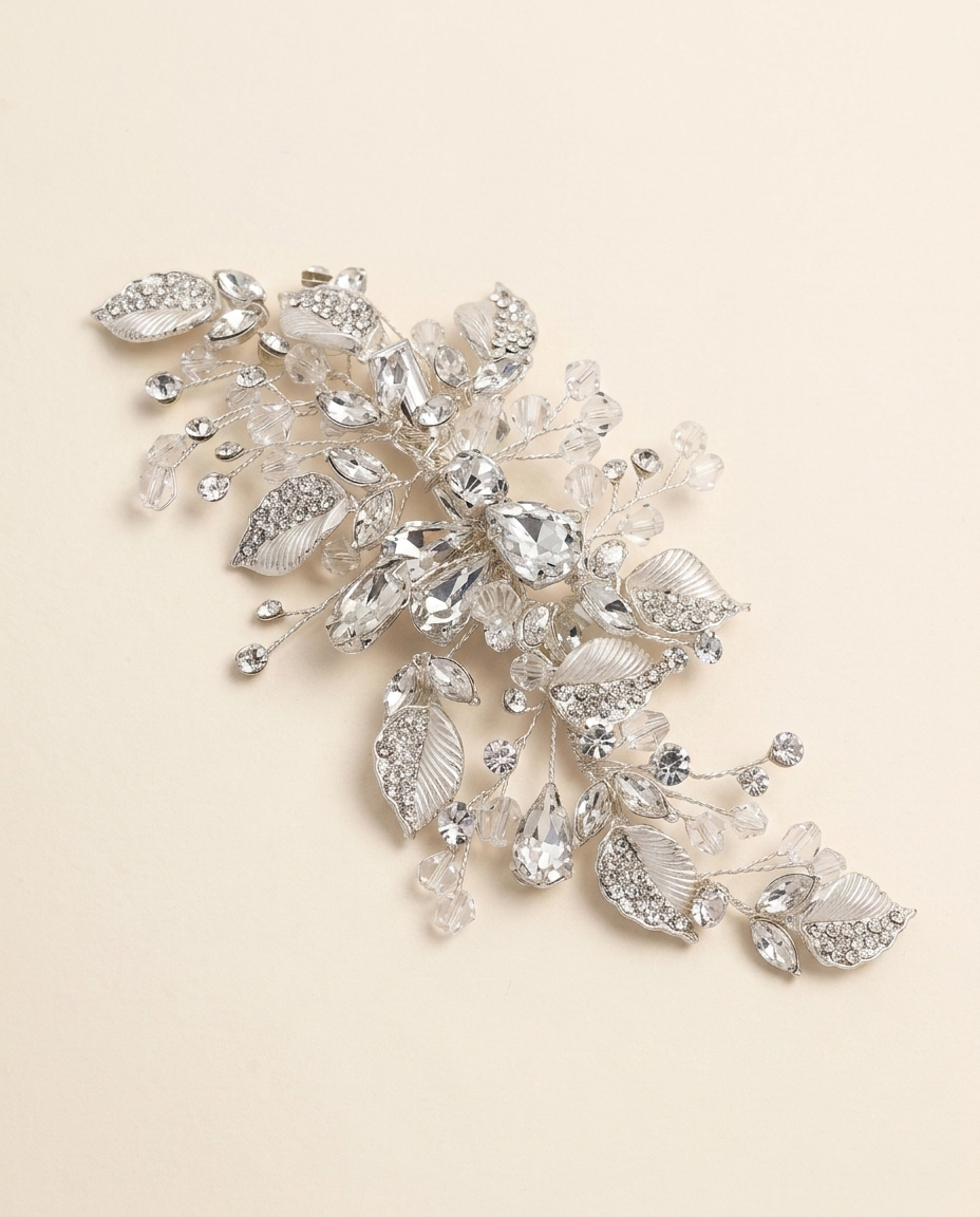 A decorative piece of jewelry with a combination of clear and silver elements, including leaves and crystals, set against a light beige background.