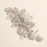 A decorative piece of jewelry with a combination of clear and silver elements, including leaves and crystals, set against a light beige background.