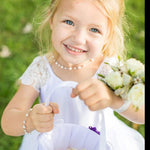 A young girl in a white dress holding a white flower basket and a bouquet of white flowers, smiling brightly.