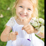 A young girl in a white dress holding a white flower basket and a bouquet of white flowers, smiling brightly.