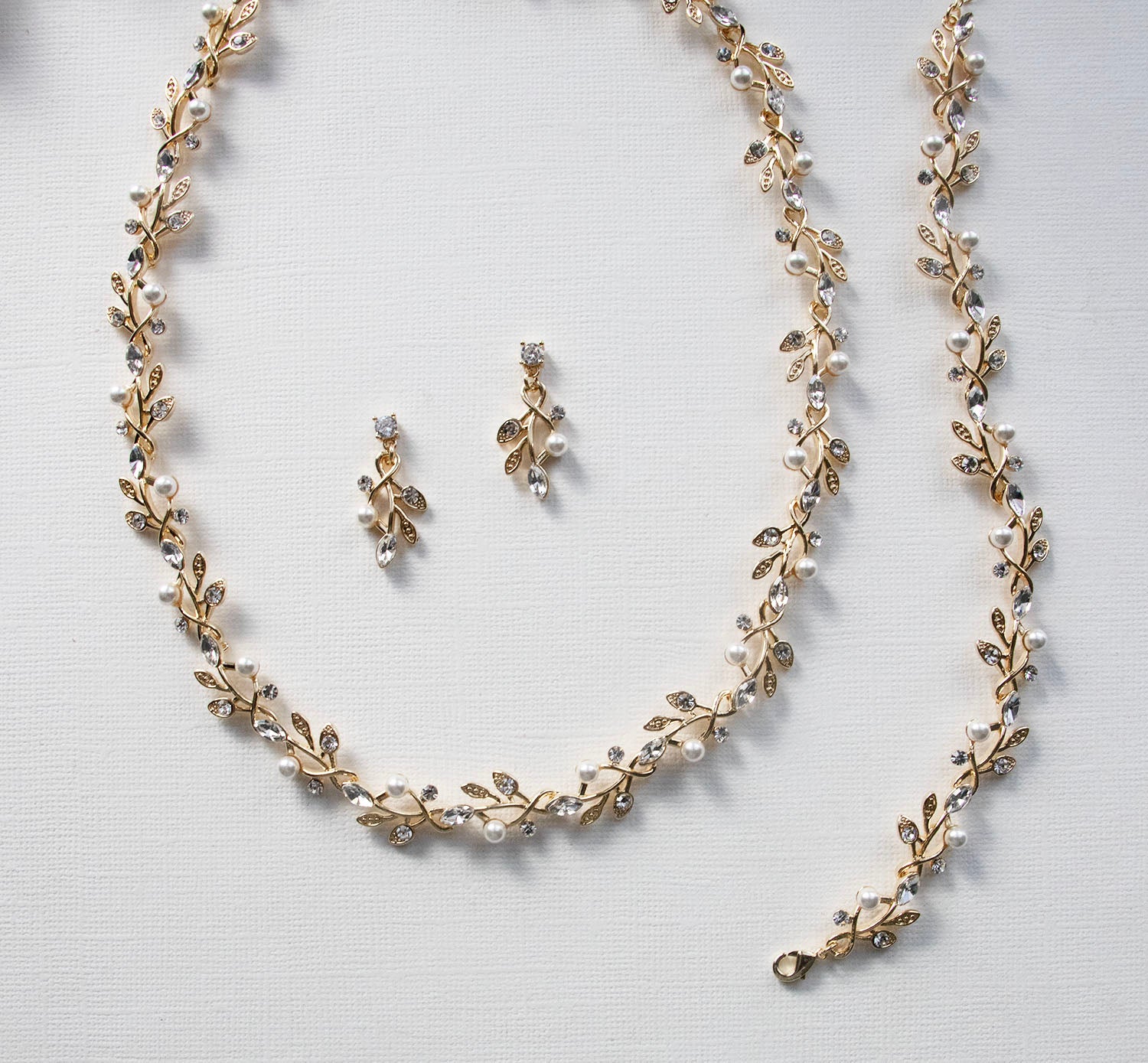 A delicate gold necklace with leaf-shaped pendants and a matching earring set, all adorned with small pearls and crystals.